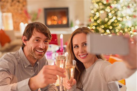 Smiling couple toasting champagne flutes and taking selfie at Christmas dinner table Stock Photo - Premium Royalty-Free, Code: 6124-08926919