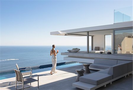 people house backside - Woman on sunny modern, luxury home showcase exterior patio with ocean view Stock Photo - Premium Royalty-Free, Code: 6124-09099752