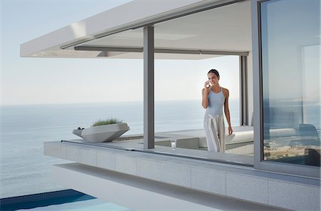 Woman talking on cell phone on modern, luxury home showcase exterior patio with ocean view Photographie de stock - Premium Libres de Droits, Code: 6124-09099755