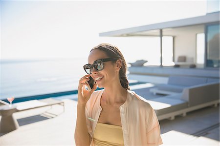 strandhaus - Smiling woman talking on smart phone on sunny modern, luxury home showcase exterior patio Stockbilder - Premium RF Lizenzfrei, Bildnummer: 6124-09099770