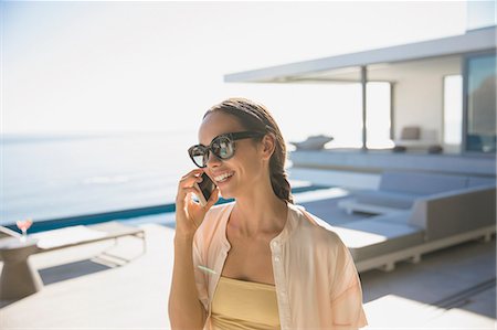 simsearch:6113-07790501,k - Smiling woman talking on smart phone on sunny modern, luxury home showcase exterior patio Stock Photo - Premium Royalty-Free, Code: 6124-09099770