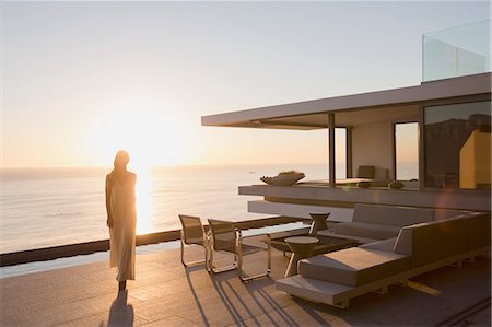 simsearch:6124-08704022,k - Woman walking on modern, luxury home showcase exterior deck with sunset ocean view Photographie de stock - Premium Libres de Droits, Code: 6124-09099729