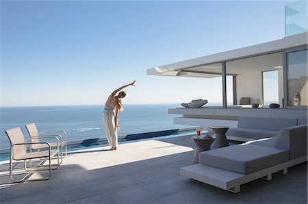 simsearch:6124-08743306,k - Woman practicing yoga side stretch on modern, luxury home showcase exterior patio with sunny ocean view Photographie de stock - Premium Libres de Droits, Code: 6124-09099861