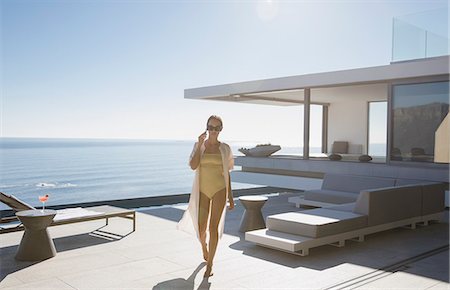 simsearch:6124-09099891,k - Woman in bathing suit walking on sunny modern, luxury home showcase exterior patio with ocean view Stock Photo - Premium Royalty-Free, Code: 6124-09099885