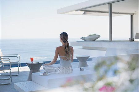 Serene woman meditating on modern, luxury home showcase exterior patio with ocean view Stock Photo - Premium Royalty-Free, Code: 6124-09099824