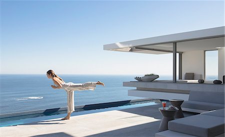 rich luxury people - Woman practicing yoga warrior 3 pose on sunny modern, luxury home showcase exterior patio with ocean view Stock Photo - Premium Royalty-Free, Code: 6124-09099837