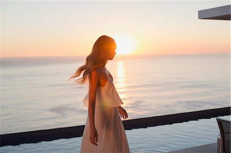 simsearch:6113-07543388,k - Woman in white dress on tranquil luxury patio with sunset ocean view Stock Photo - Premium Royalty-Free, Code: 6124-09099835