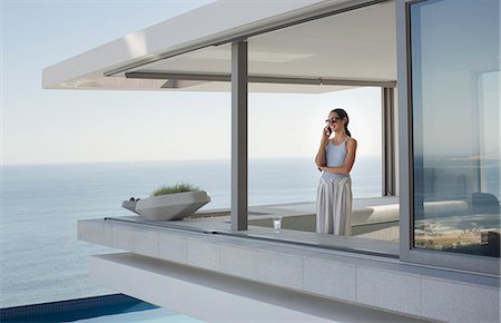 simsearch:6113-07790501,k - Woman talking on cell phone on modern, luxury home showcase exterior patio with ocean view Stock Photo - Premium Royalty-Free, Code: 6124-09099839