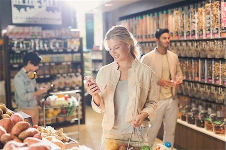 simsearch:6124-08703958,k - Young woman using cell phone, grocery shopping in market Fotografie stock - Premium Royalty-Free, Codice: 6124-09004841