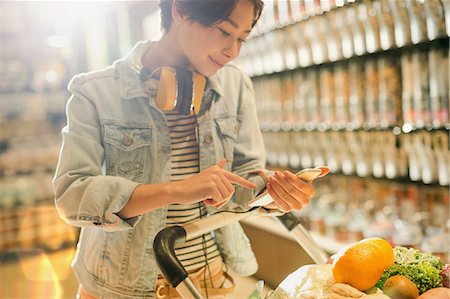 simsearch:6122-07706758,k - Young woman with headphones using cell phone in grocery store market Stock Photo - Premium Royalty-Free, Code: 6124-09004865