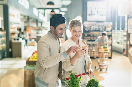 retailer - Young couple using cell phone, grocery shopping in grocery store market Stock Photo - Premium Royalty-Free, Code: 6124-09004889