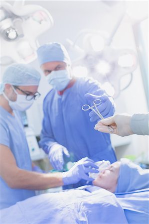 Surgeon reaching for surgical scissors in operating room Photographie de stock - Premium Libres de Droits, Code: 6124-09026363