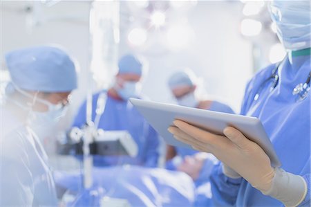 Surgeon wearing rubber gloves, using digital tablet in operating room Stock Photo - Premium Royalty-Free, Code: 6124-09026373