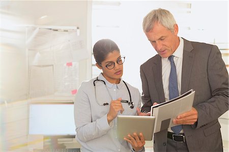 Female doctor and male hospital administrator talking, looking at digital tablet and paperwork in examination room Stock Photo - Premium Royalty-Free, Code: 6124-09026400