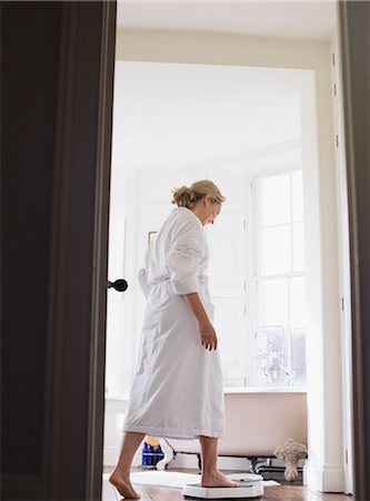 Mature woman in bathrobe stepping on bathroom scale Foto de stock - Sin royalties Premium, Código: 6124-09143720