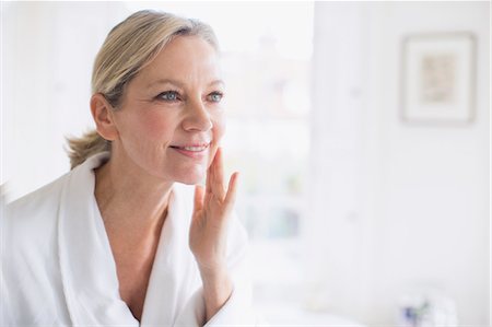 simsearch:649-02198955,k - Smiling mature woman applying moisturizer to face at bathroom mirror Foto de stock - Sin royalties Premium, Código: 6124-09143722