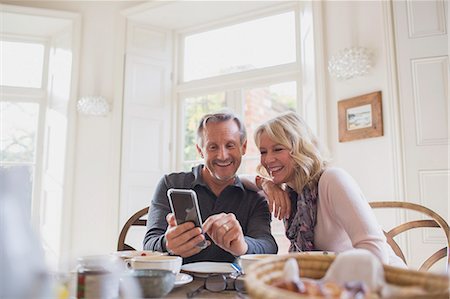 Smiling mature couple using smart phone at dining table Photographie de stock - Premium Libres de Droits, Code: 6124-09143724