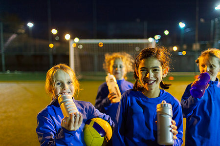 Portrait smiling girls soccer team taking a break from practice, drinking water on field at night Stock Photo - Premium Royalty-Free, Code: 6124-09197418