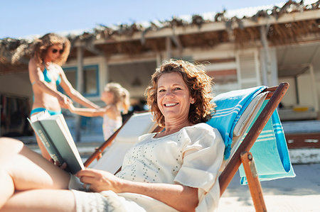 family beach house - Portrait happy woman reading book, relaxing on sunny beach Stock Photo - Premium Royalty-Free, Code: 6124-09269549