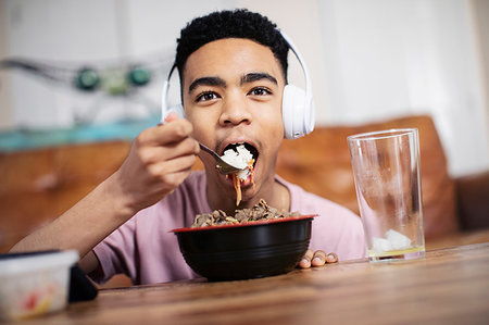 dinner live music - Portrait teenage boy with headphones eating at coffee table Stock Photo - Premium Royalty-Free, Code: 6124-09269948