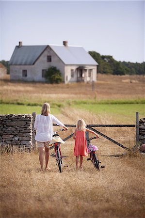 simsearch:6102-03828809,k - Sweden, Gotland, Faro, Mother and daughter (8-9) wheeling bicycles toward farm gate Stock Photo - Premium Royalty-Free, Code: 6126-08642799