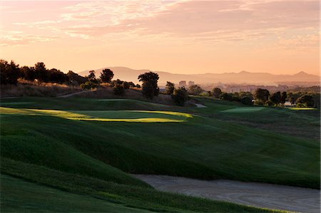 Spain. Barcelona, Real Club de Golf El Prat, Grassy hills of golf course in shadow with distant cityscape in background Stock Photo - Premium Royalty-Free, Code: 6126-08644413