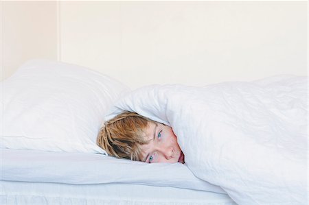 Finland, Helsinki, Portrait of young man lying in bed under white blanket Stock Photo - Premium Royalty-Free, Code: 6126-08659491