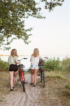 Sweden, Blekinge, Hallevik, Rear view of two teenage girls(14-15, 16-17) walking with bicycles Stock Photo - Premium Royalty-Free, Code: 6126-08636184