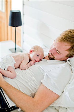 family laying in bed together - Sweden, Mid-adult man looking at his baby boy (0-1 months) in bedroom Stock Photo - Premium Royalty-Free, Code: 6126-08636109