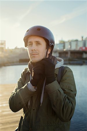 scudo - Sweden, Sodermanland, Stockholm, Sodermalm, Slussen, Outdoor portrait of mid adult man tying helmet strap Fotografie stock - Premium Royalty-Free, Codice: 6126-08636133