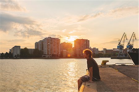 Finland, Helsinki, Uusimaa, Sompasaari, Man sitting on pier at sunset Stock Photo - Premium Royalty-Free, Code: 6126-08636704