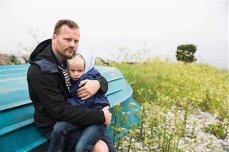 simsearch:6126-08636742,k - Sweden, Gotland. Mature man sitting on boat turned upside down and holding boy (6-7) Stock Photo - Premium Royalty-Free, Code: 6126-08781174