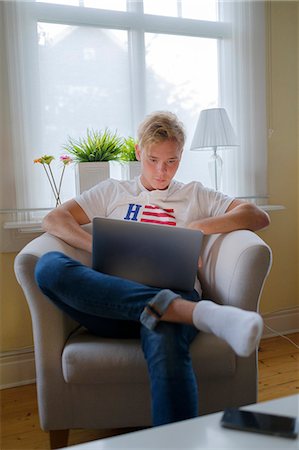 simsearch:6126-08644046,k - Young man sitting in armchair and using laptop Stock Photo - Premium Royalty-Free, Code: 6126-09102650