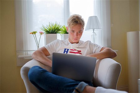 simsearch:6126-08644046,k - Young man sitting in armchair and using laptop Stock Photo - Premium Royalty-Free, Code: 6126-09102651