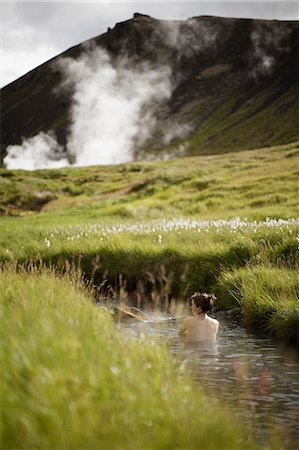 Woman bathing in stream in Iceland with geyser and mountain in background Stock Photo - Premium Royalty-Free, Code: 6126-09102729