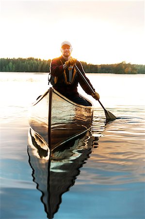 ethnic person baseball cap - Man paddling canoe on lake Stock Photo - Premium Royalty-Free, Code: 6126-09103726