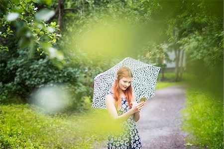 simsearch:6126-08781229,k - Woman wearing floral dress standing with umbrella in park Photographie de stock - Premium Libres de Droits, Code: 6126-09104242