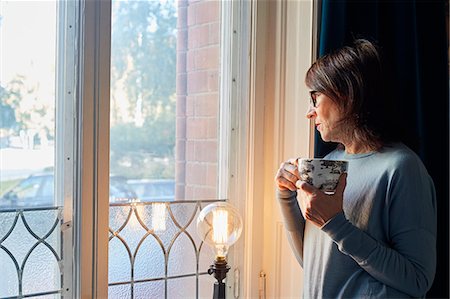 simsearch:649-09123654,k - Woman looking through window and holding coffee cup Photographie de stock - Premium Libres de Droits, Code: 6126-09104288