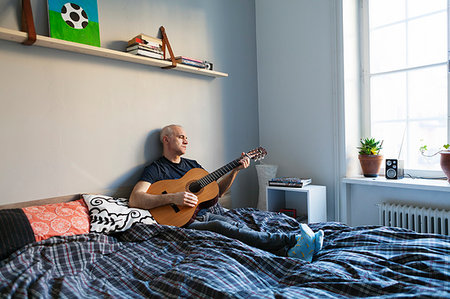 Senior man playing guitar on bed Foto de stock - Sin royalties Premium, Código: 6126-09266261