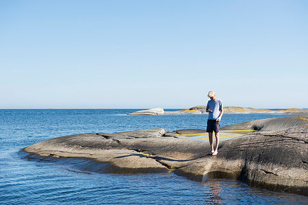 simsearch:6126-09266702,k - Young man standing on rocks by sea Fotografie stock - Premium Royalty-Free, Codice: 6126-09266288