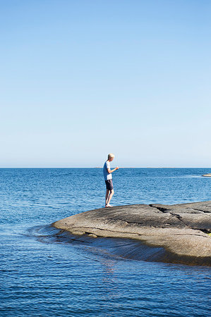 simsearch:6126-09266702,k - Young man standing on rocks by sea Fotografie stock - Premium Royalty-Free, Codice: 6126-09266289