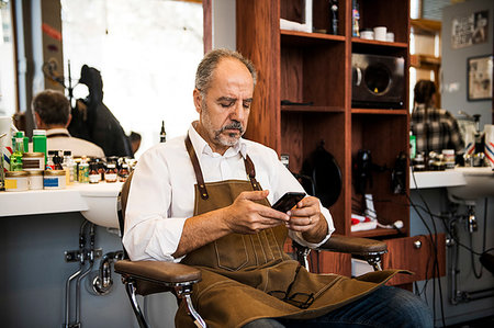 Barber using smartphone in barbershop Stock Photo - Premium Royalty-Free, Code: 6126-09268218
