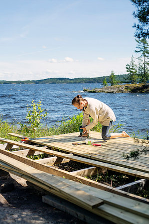 Mid adult woman building a deck in front of a lake in Finland Stock Photo - Premium Royalty-Free, Code: 6126-09204670