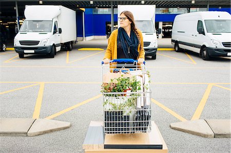Young woman pushing trolley full of purchases in car park Photographie de stock - Premium Libres de Droits, Code: 6127-08667378