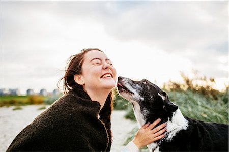 Cheerful young woman playing with dog on beach against sky Foto de stock - Sin royalties Premium, Código: 6127-08687856