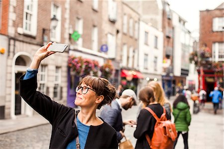 Smiling woman taking selfie with friends standing in background on city street Stock Photo - Premium Royalty-Free, Code: 6127-08687985