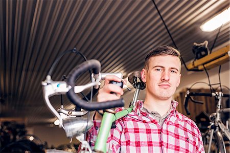 Portrait of confident mechanic carrying bicycle in workshop Stock Photo - Premium Royalty-Free, Code: 6127-08688188