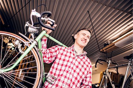 Low angle view of happy mechanic carrying bicycle in shop Stock Photo - Premium Royalty-Free, Code: 6127-08688189