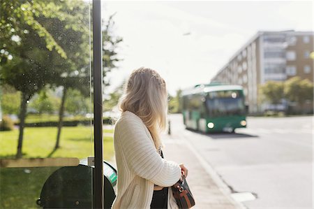 Young woman carrying shoulder bag standing near garbage bin looking at bus Stock Photo - Premium Royalty-Free, Code: 6127-08688709