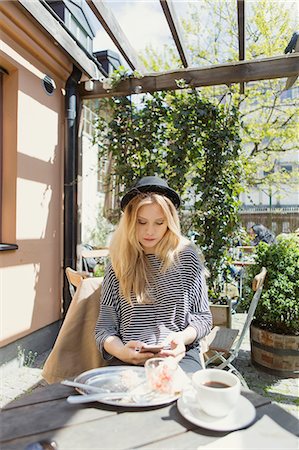 restes - Young woman wearing hat using phone while having coffee at cafe Photographie de stock - Premium Libres de Droits, Code: 6127-08688732